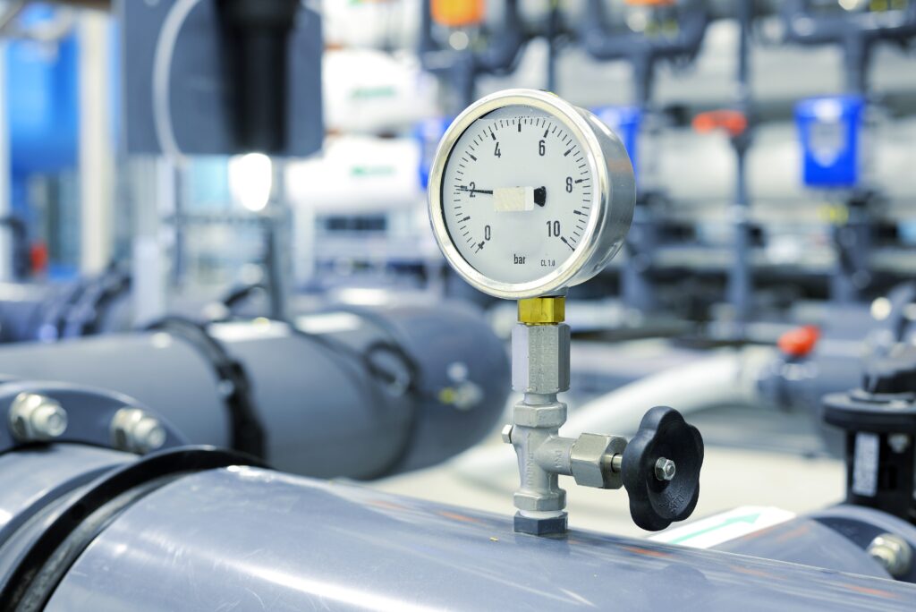 Das Bild zeigt eine Druckluftanzeiger angebracht an Rohren, die durch eine saubere Farbrikhalle führen